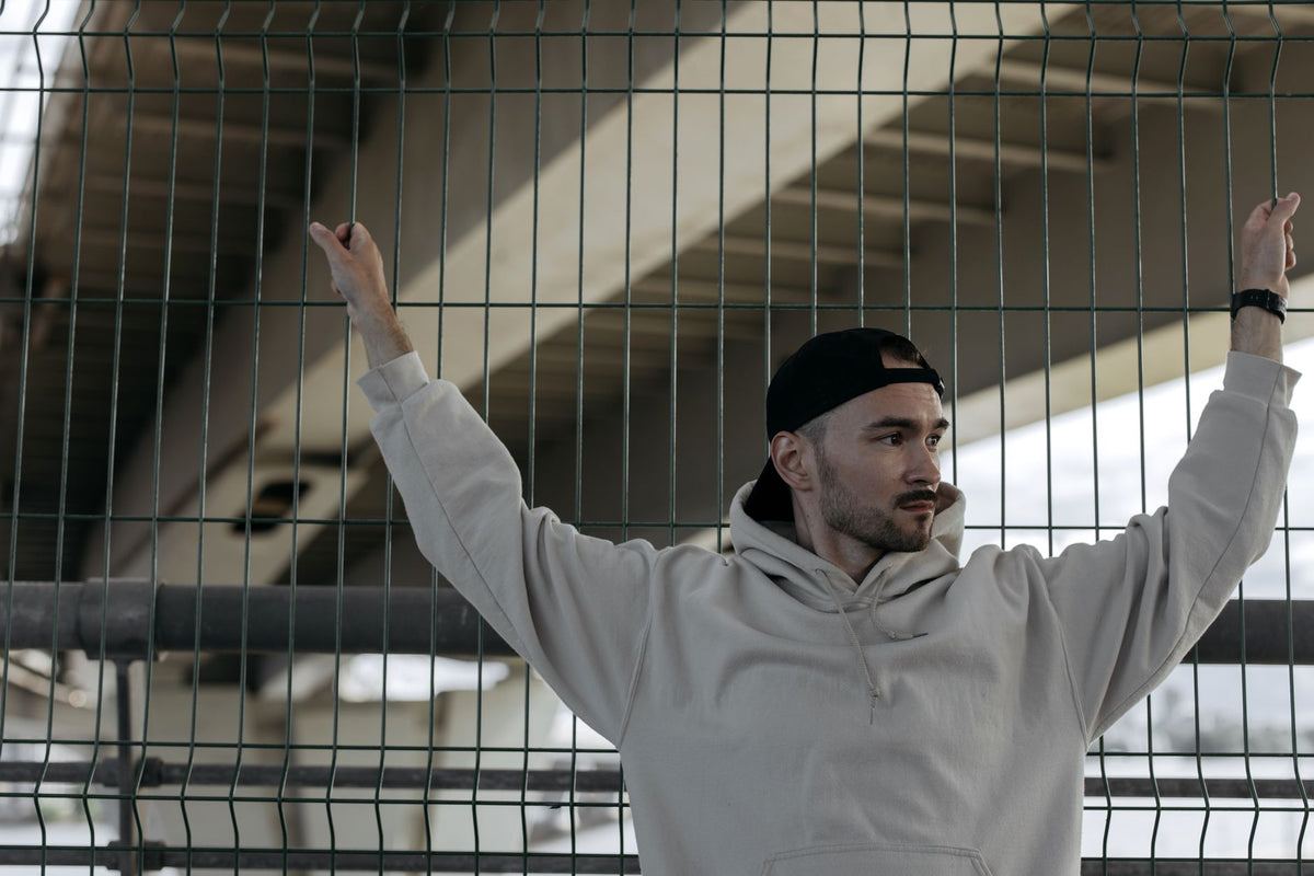 Jeune homme en sweat à capuche oversize de style Y2K, bras levés sous un pont urbain