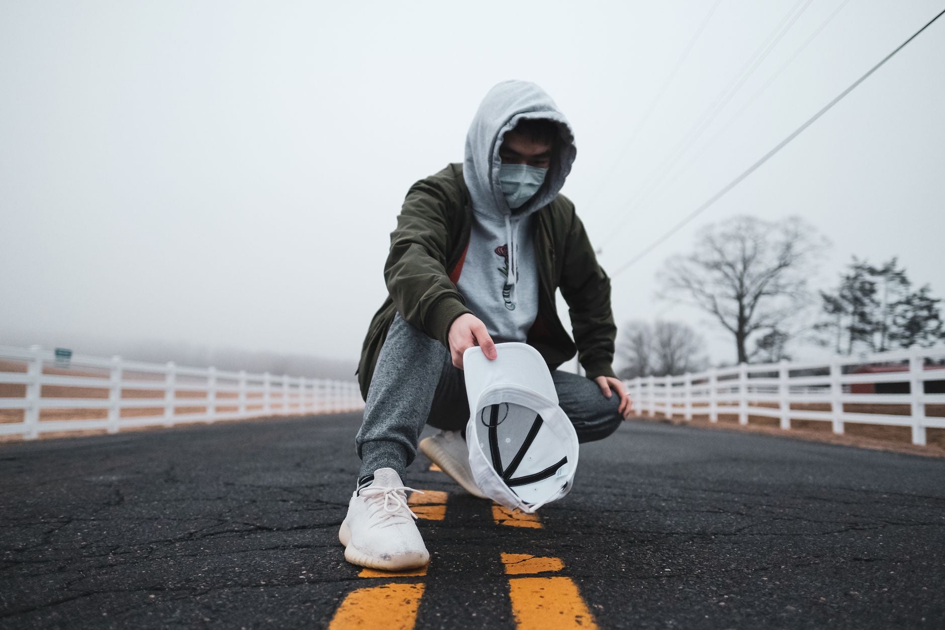 Jeune homme en hoodie tenant une casquette blanche sur une route brumeuse en style urbain
