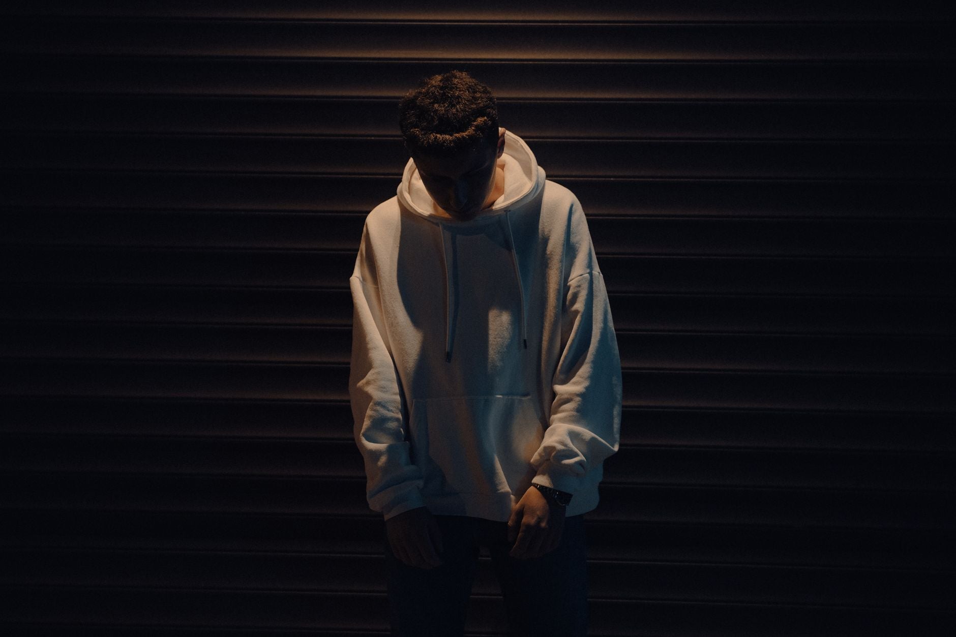 Jeune homme en sweat oversize blanc posant devant un rideau métallique urbain la nuit