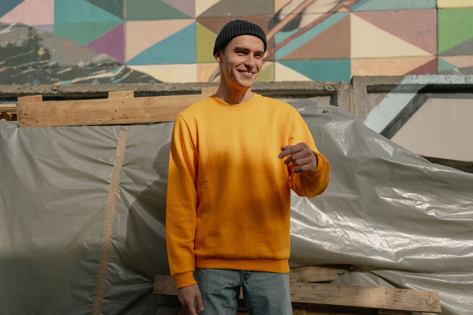 Jeune homme souriant en pull jaune uni devant un mur street art coloré