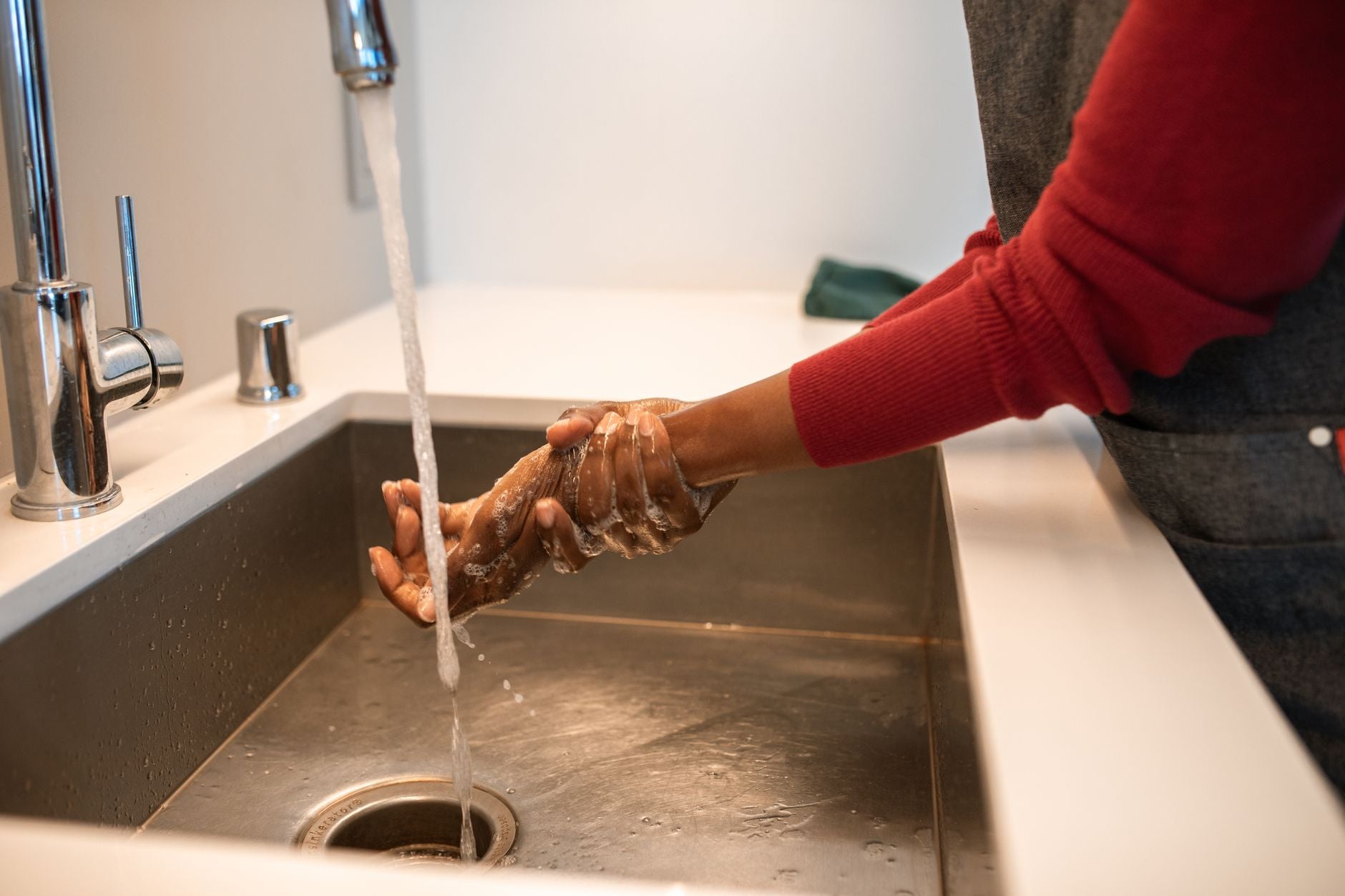 Mains rinçant délicatement un pull en maille rouge sous l'eau courante d'un évier