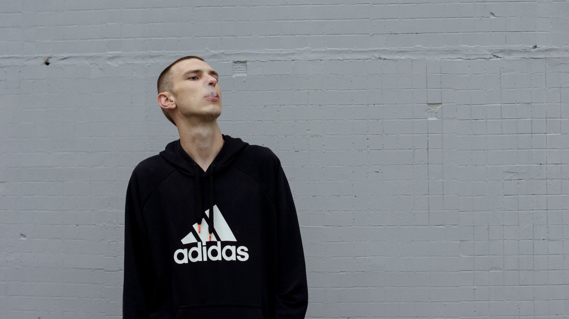 Jeune homme portant un hoodie oversize gris qui tombe sur ses sneakers blanches en look streetwear urbain