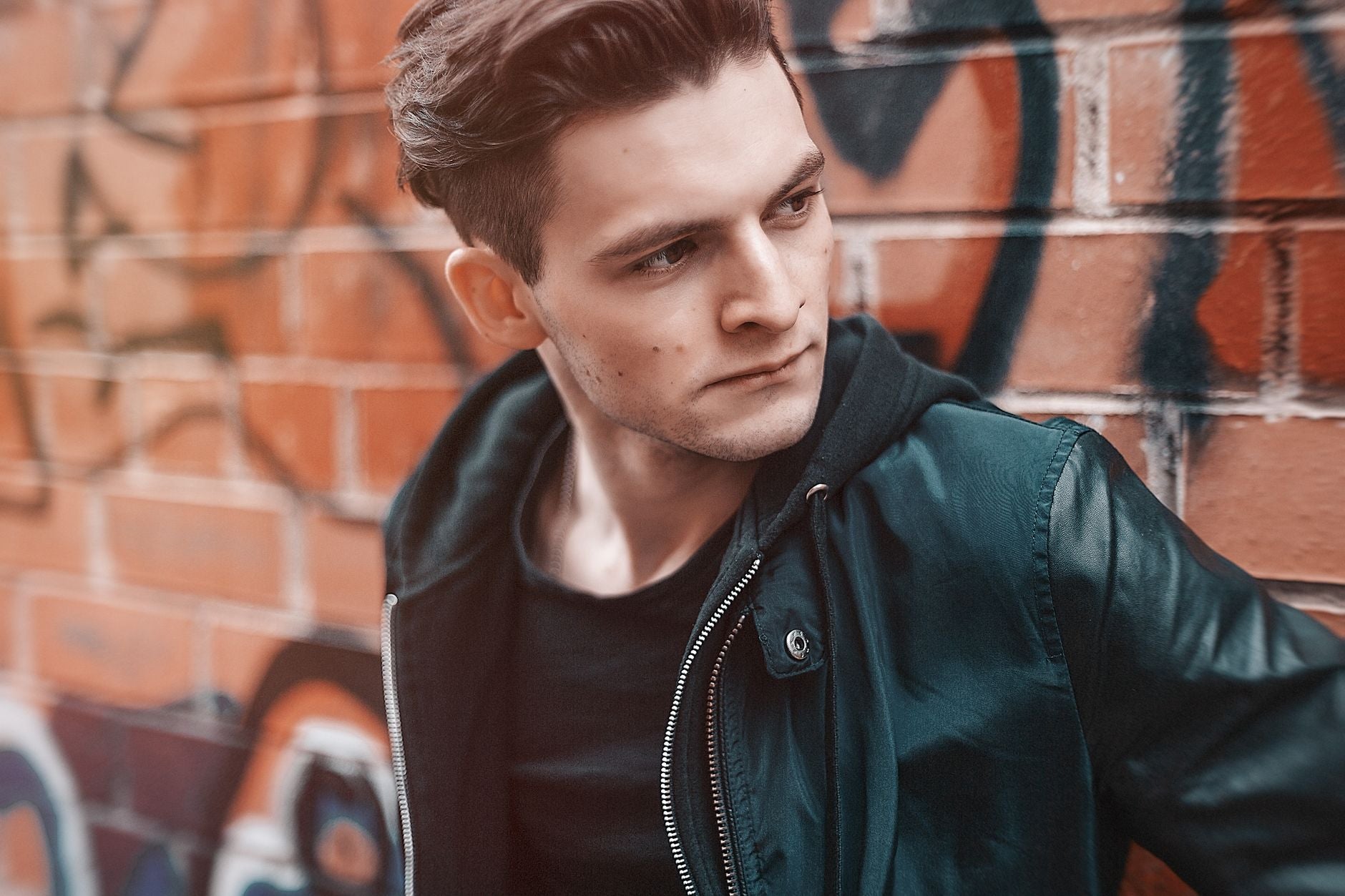Jeune homme en blouson streetwear vert posant devant un mur graffiti urbain