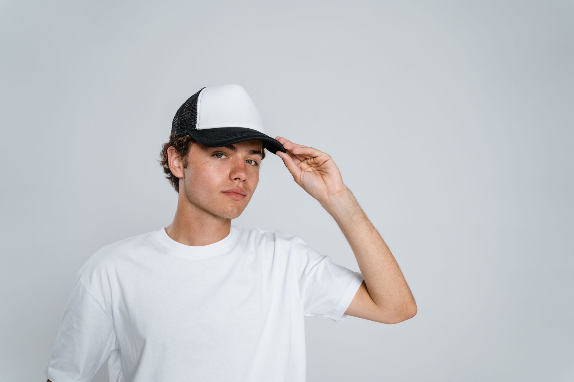 Jeune homme en t-shirt blanc ajustant sa casquette bicolore sans logo visible